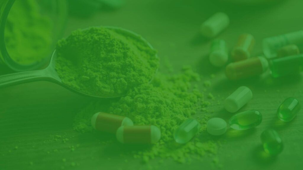 A close-up of vibrant green spirulina powder spilling from a spoon, with tablets and capsules scattered on a wooden table, soft natural lighting.
